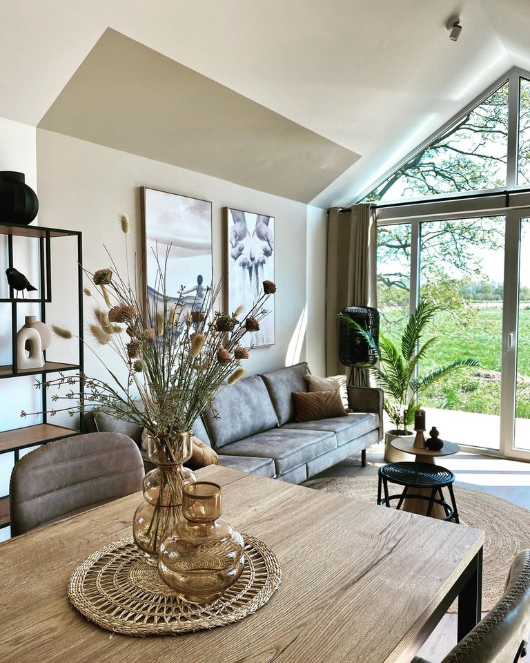 Interieur met een houten eettafel, glazen vazen en een zithoek bij het raam